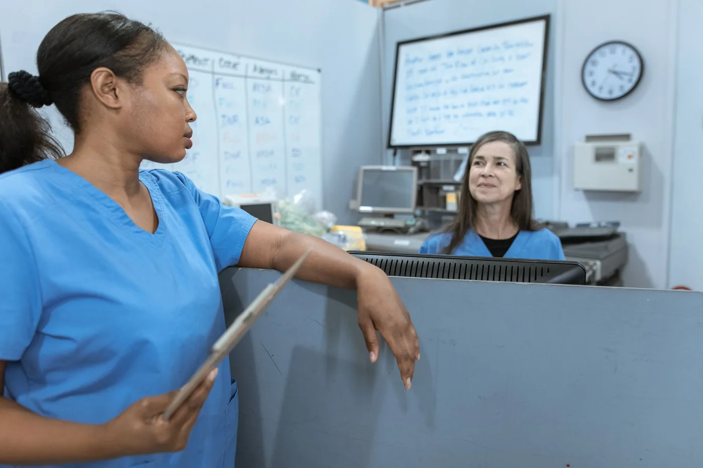 Nurse in blue scrubs talking with a colleague at a hospital nurses' station