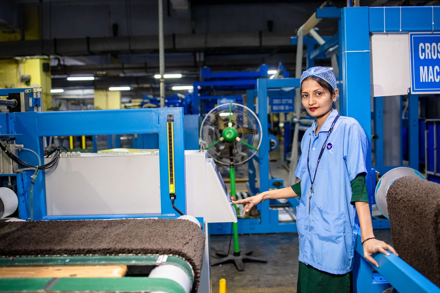 Factory worker in a hairnet and scrubs standing beside textile machinery during a 12-hour shift