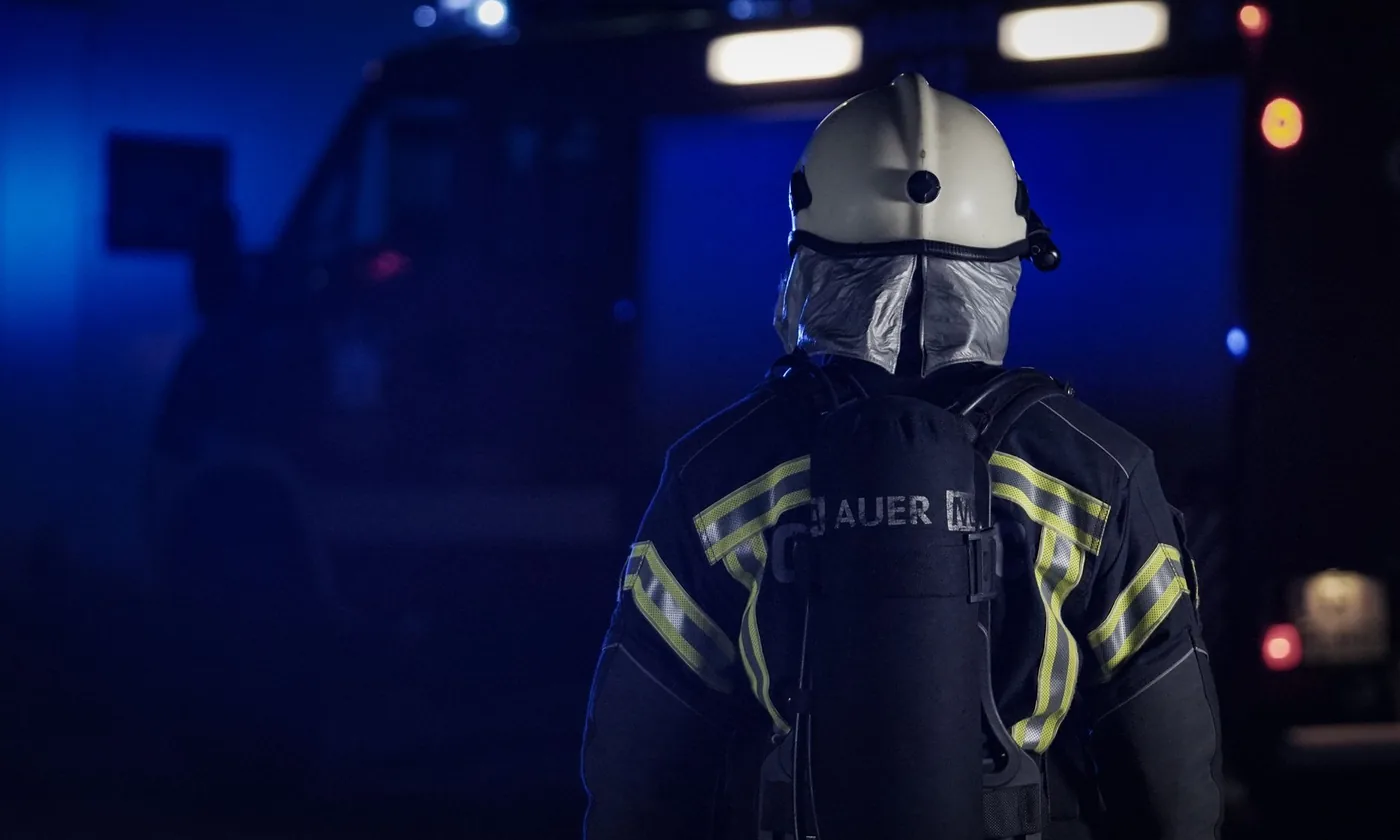 Firefighter in turnout gear and helmet standing beside a fire engine at night