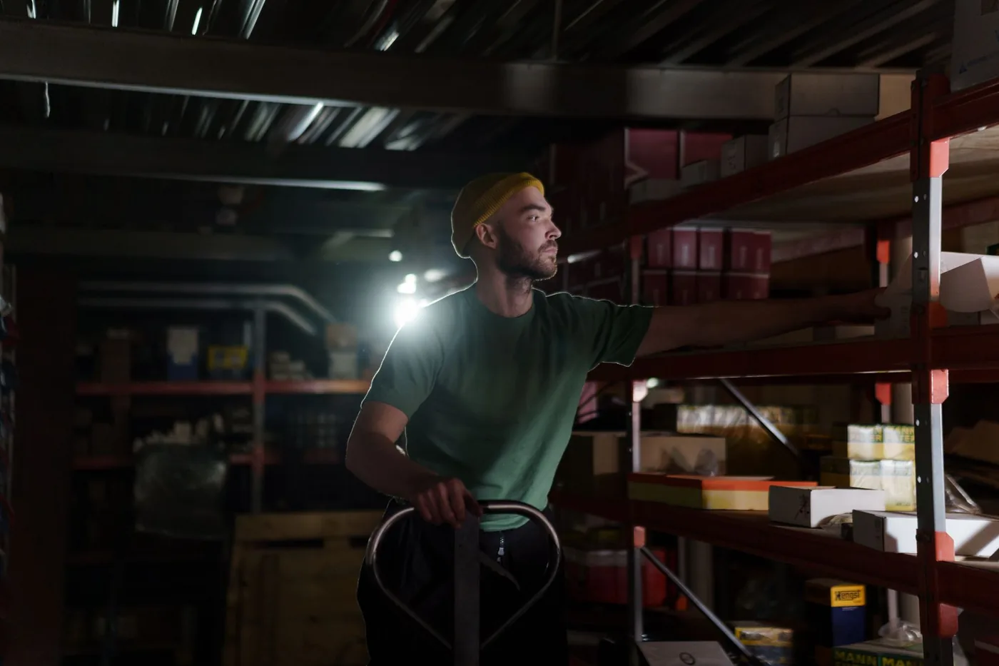 Warehouse worker with a headlamp moving stock along dark storage shelves