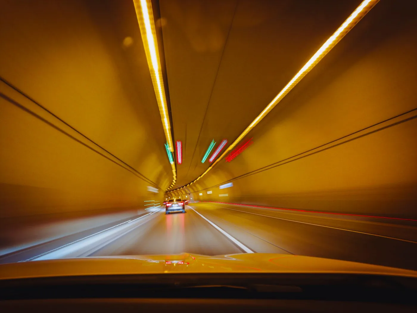 Blurry traffic scene with cars speeding through a brightly lit tunnel at night.