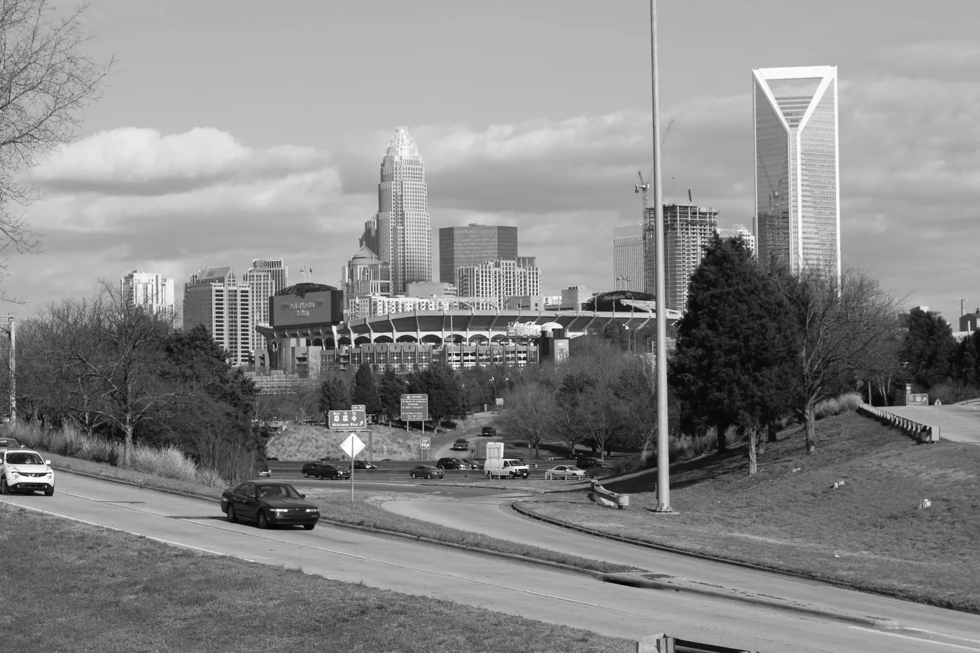 A black and white photograph of Charlotte's skyline featuring roads and moving vehicles.