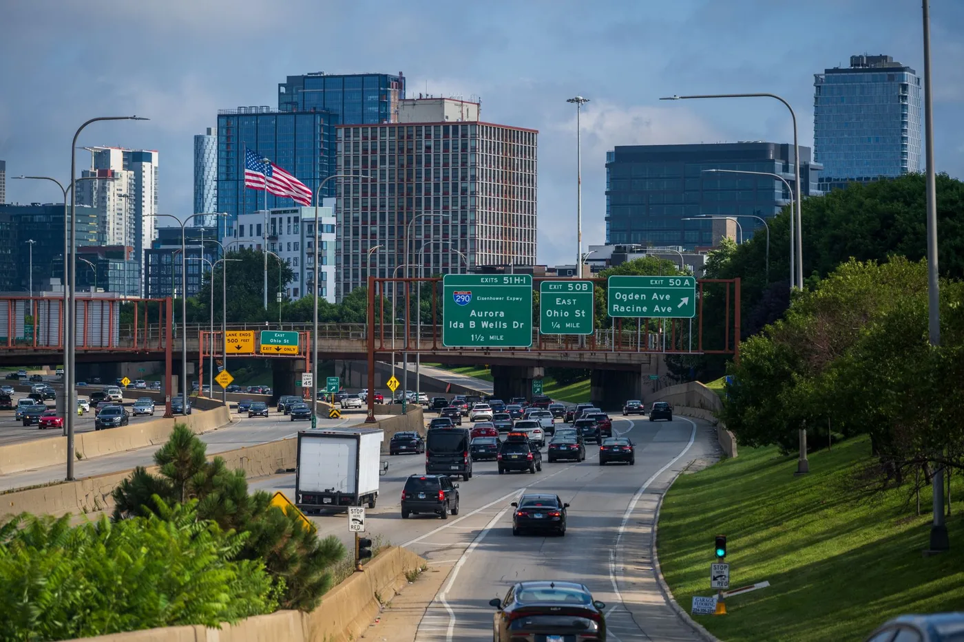 Traffic flows on a Chicago highway with a backdrop of modern skyscrapers and clear signage.