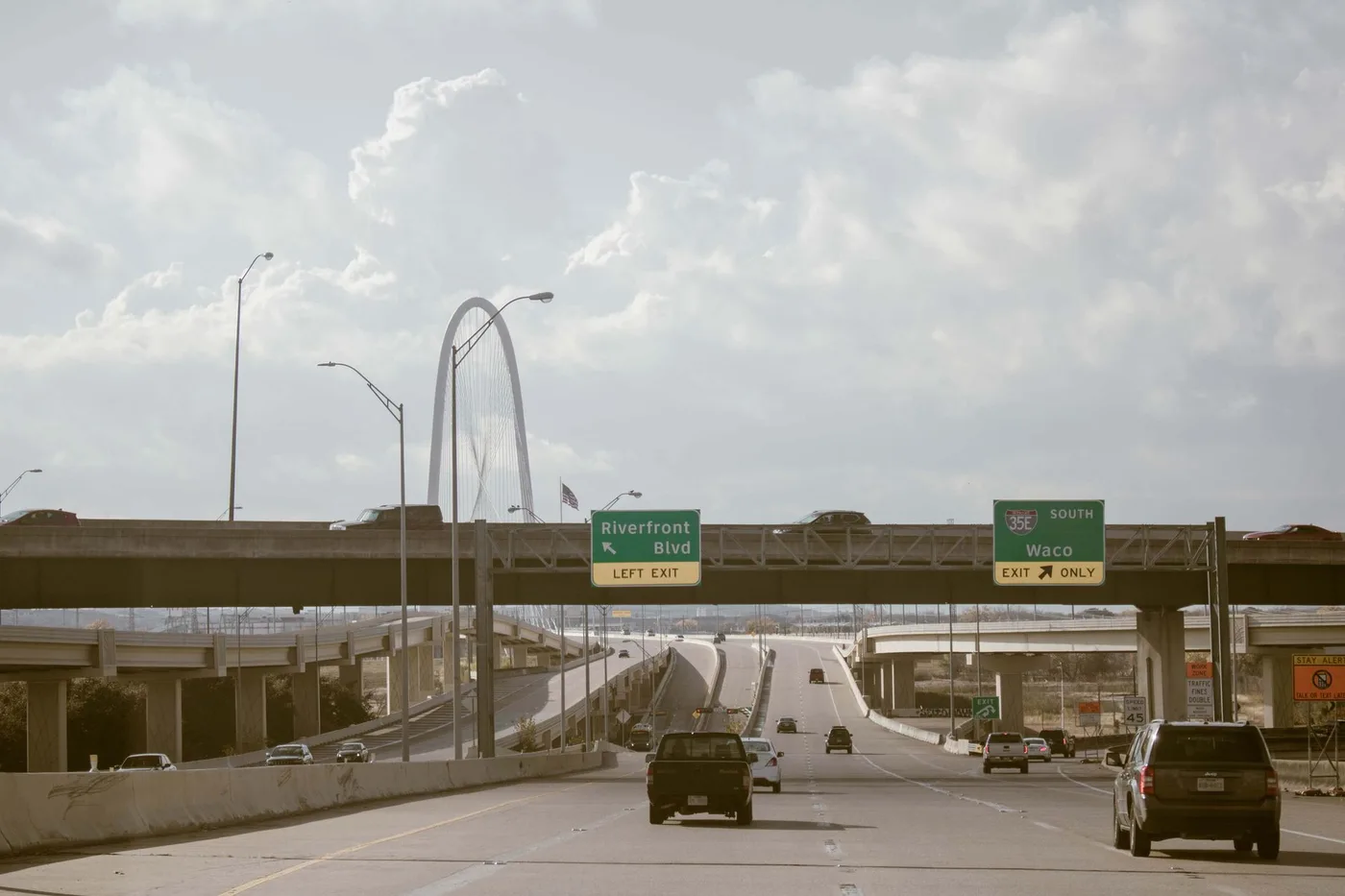 Daytime view of a busy expressway in Dallas, Texas featuring cars and road signs.