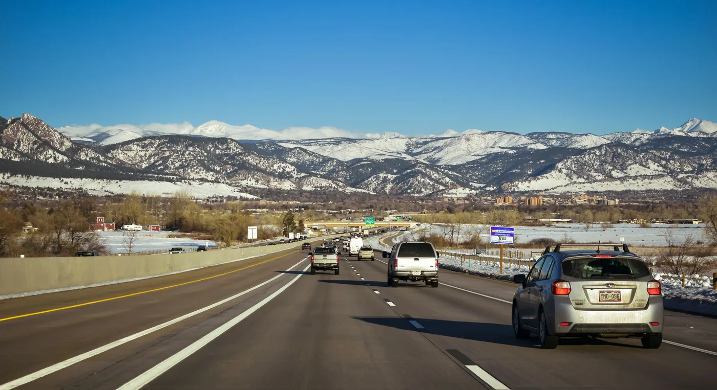 A scenic highway view surrounded by snow-capped mountains under a clear blue sky, showcasing traffic flow in Colorado.