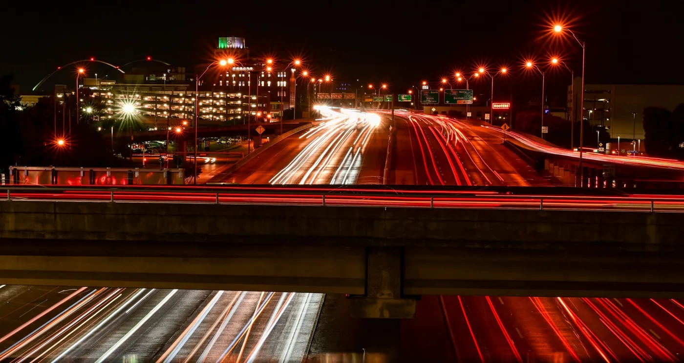 Long exposure shot capturing vibrant traffic light trails on a Dallas highway at night.
