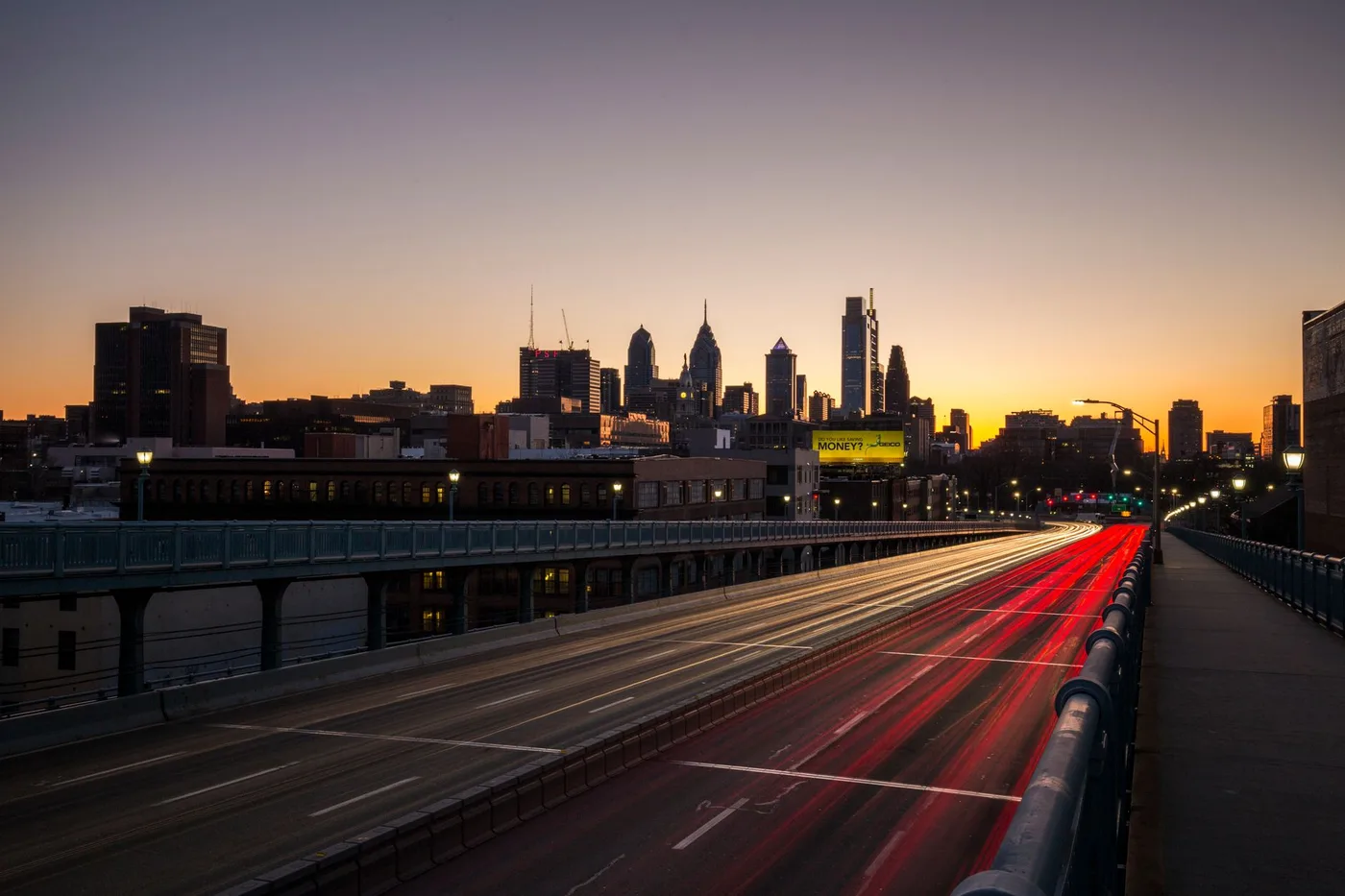 Philadelphia skyline captured at twilight with vibrant light trails on the highway, showcasing urban life.