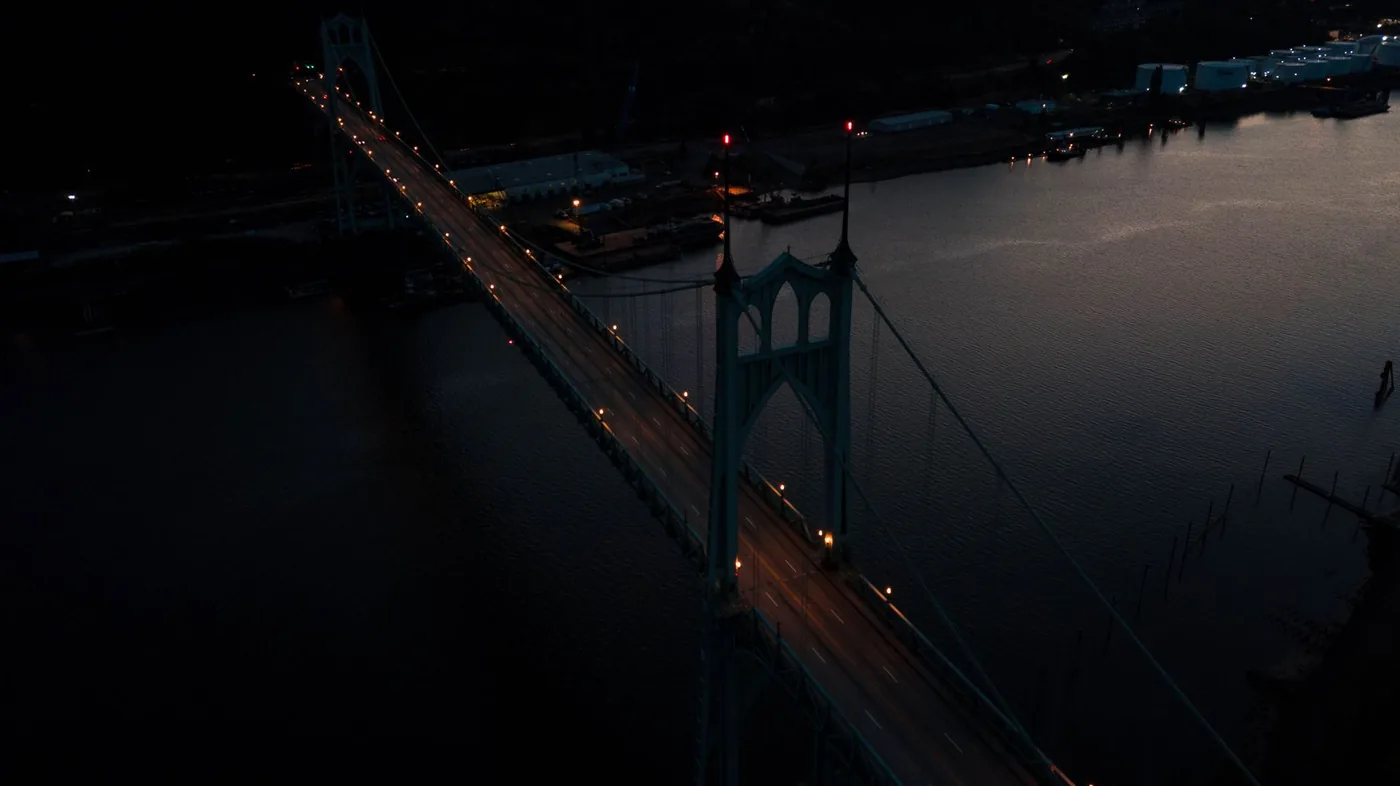 A stunning aerial shot of Portland's St. Johns Bridge lit up at night, spanning the Willamette River.