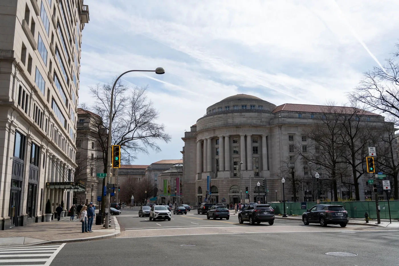 Traffic and pedestrians on a street with historic architecture in Washington DC on a clear day.