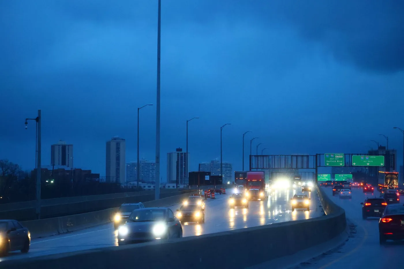 Traffic flows on a Chicago highway at dusk, featuring a city skyline under a moody blue sky.