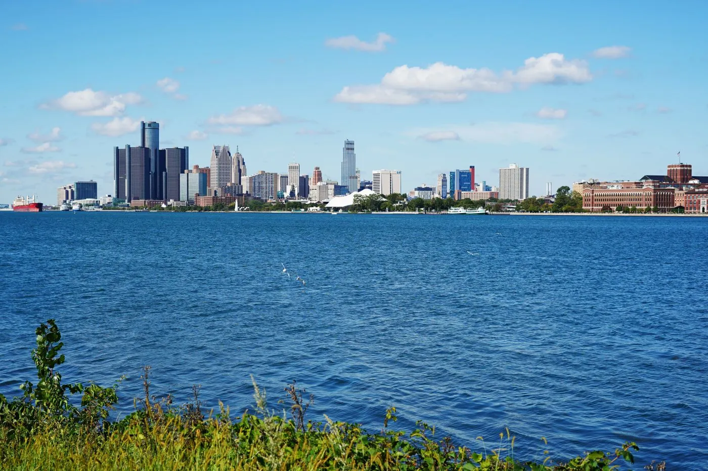 Panoramic view of Detroit skyline across the river, showcasing iconic buildings on a sunny summer day.