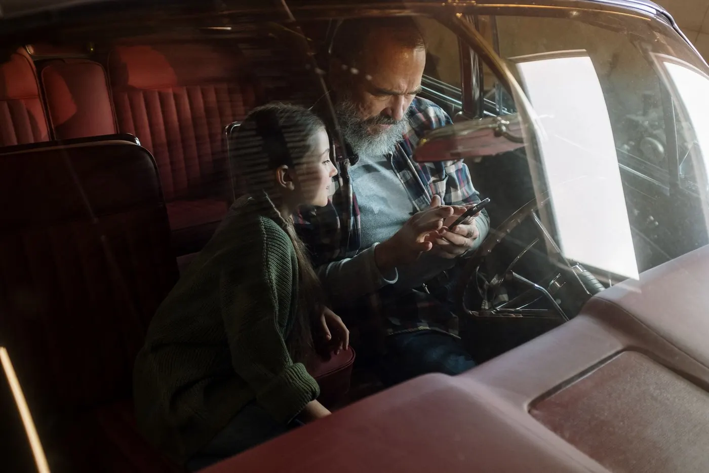 A father and daughter sitting in a car, looking at a phone together.