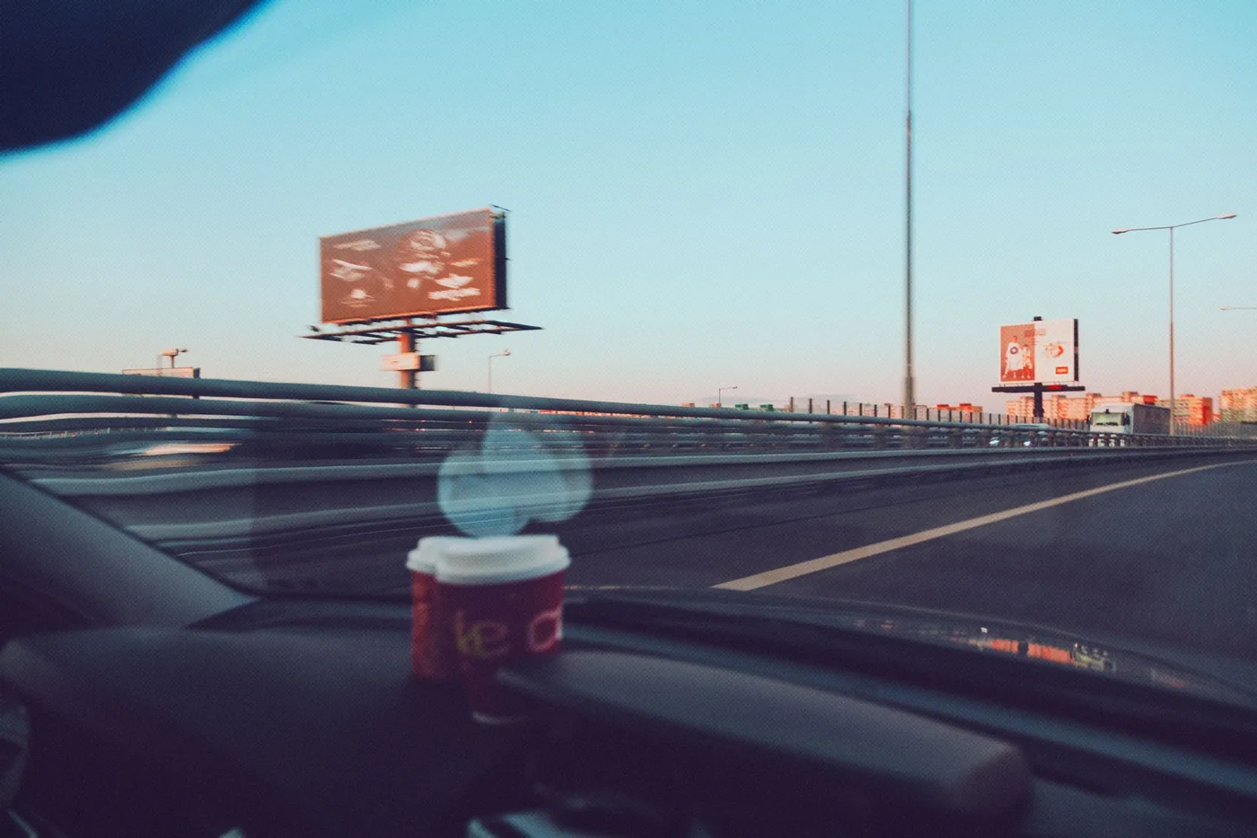 A peaceful road trip at sunset captured from a car in Slovakia, featuring coffee on the dashboard.