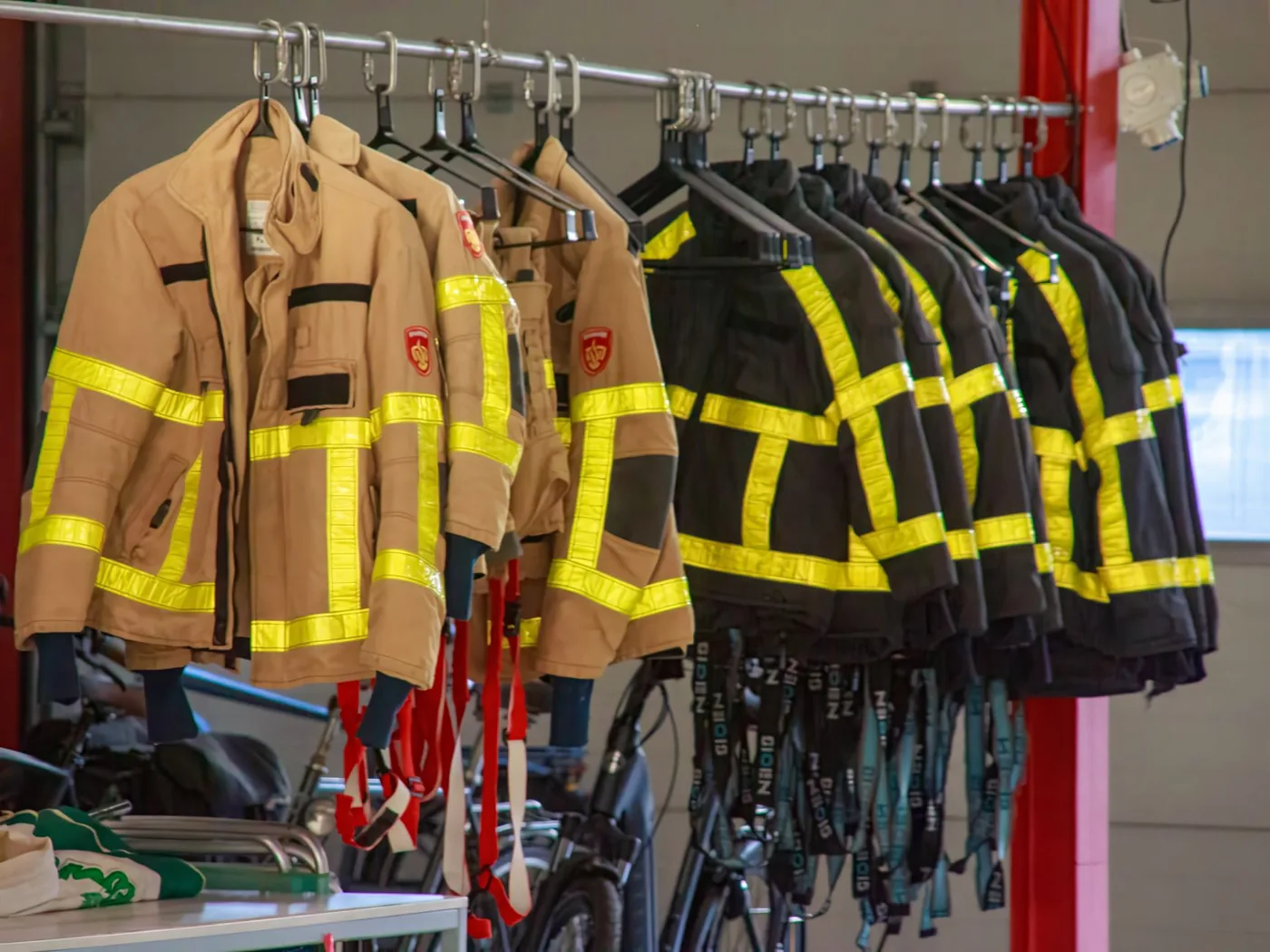 Firefighter jackets with reflective strips hanging in a fire station, ready for the next shift.