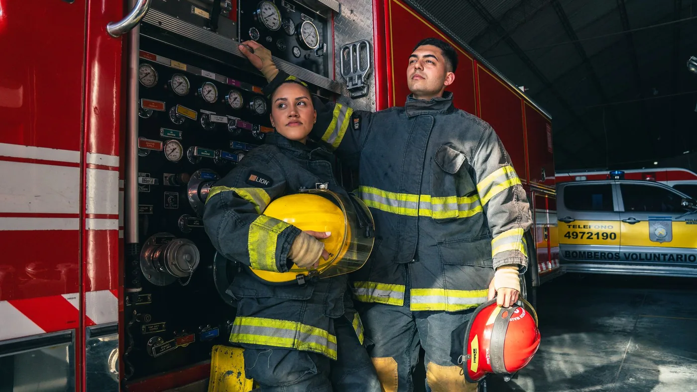 Two firefighters in full turnout gear standing beside a fire truck inside the station