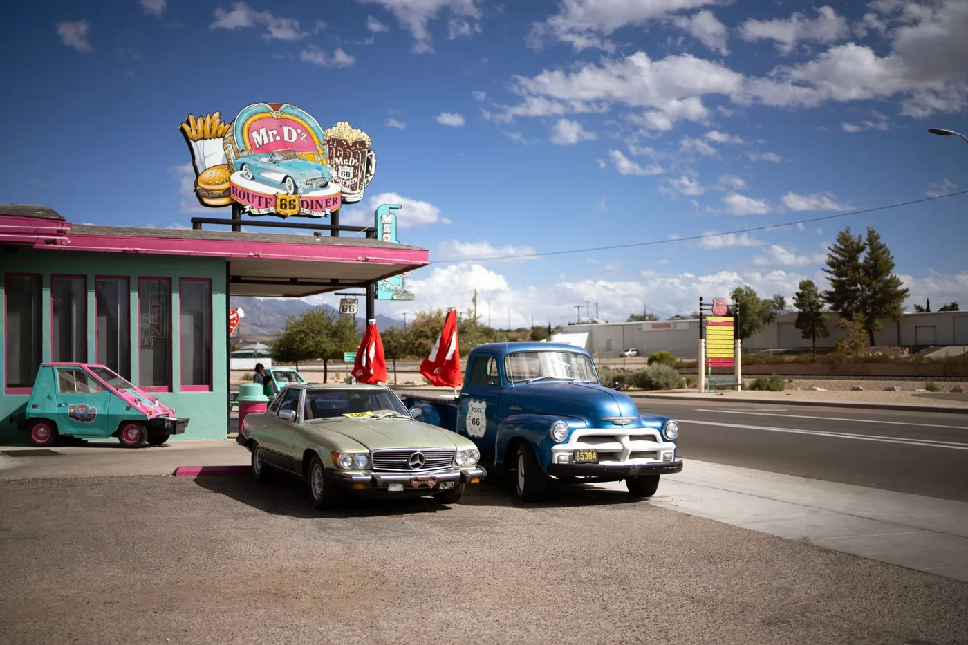 Vintage cars parked outside Mr. D's Route 66 Diner under a bright blue sky.