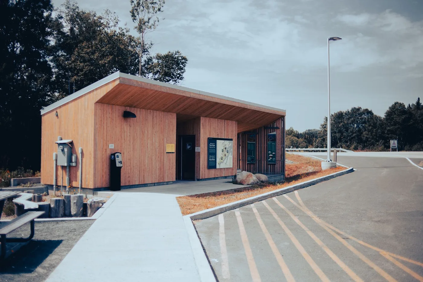 Wooden building at a roadside rest area with parking under a clear sky.