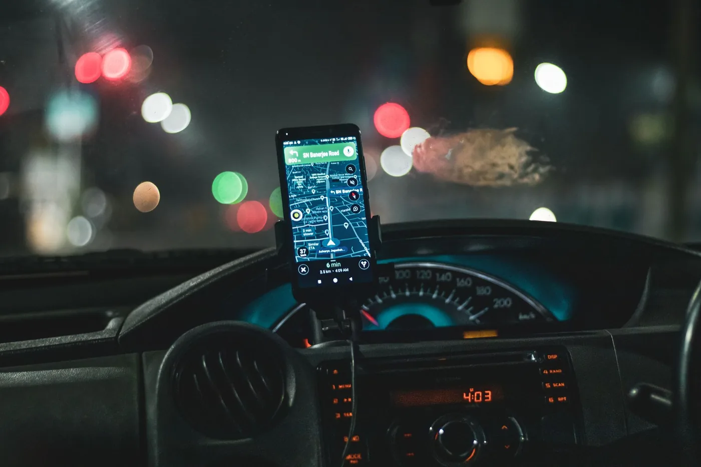 Close-up of a smartphone showing map navigation inside a car at night.