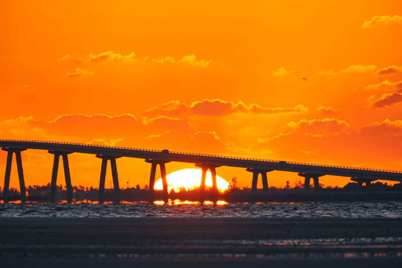 Stunning sunset view of a bridge over water in Florida, showcasing vivid orange skies and reflections.