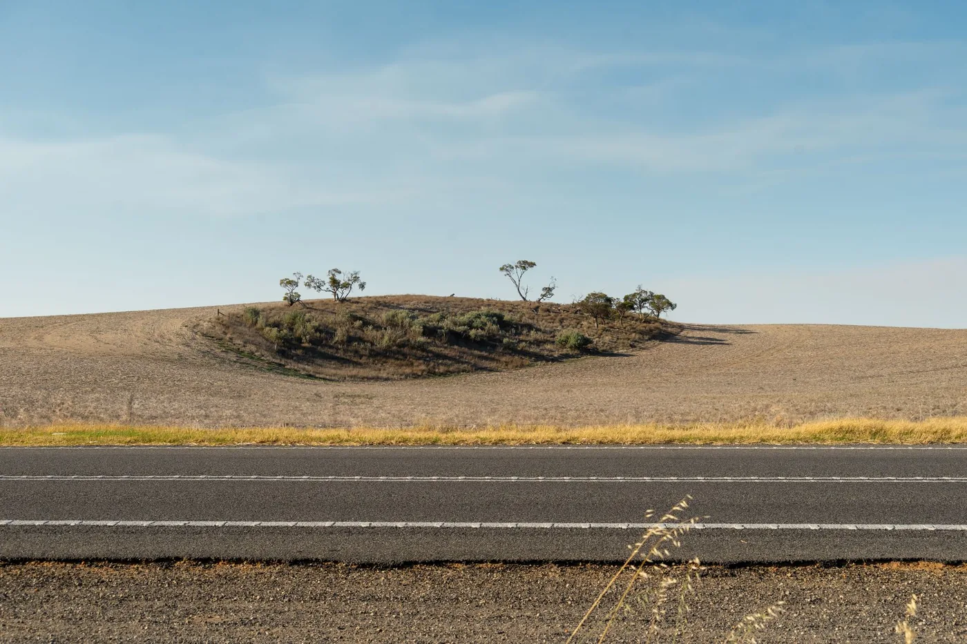 Serene view of an empty road against rolling hills under a clear sky.