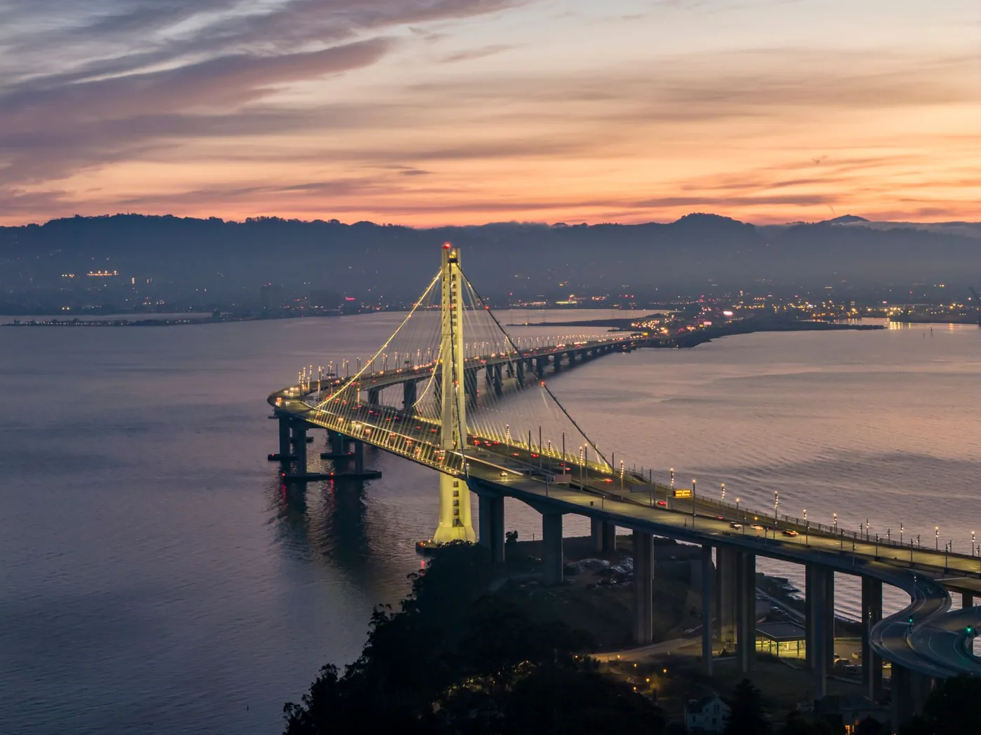 Aerial view of Bay Bridge at twilight with vibrant sunset and cityscape.