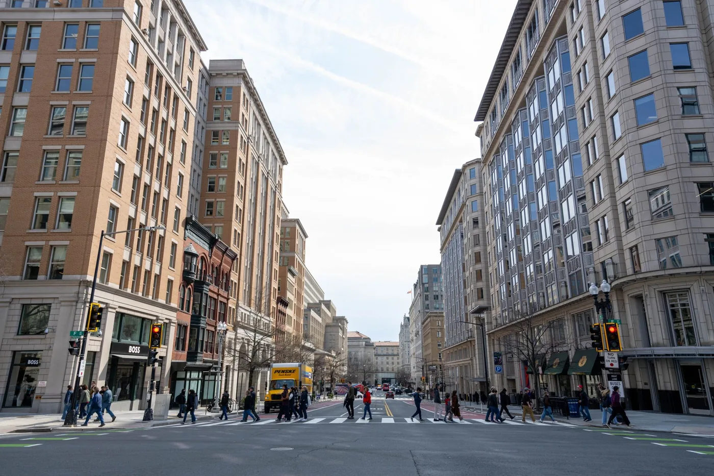 Downtown Washington DC road with high-rise buildings and pedestrians crossing.