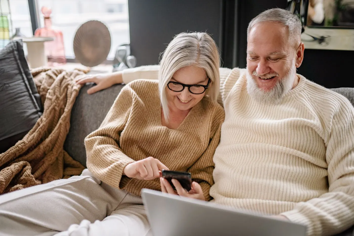 A smiling older couple on a sofa looking at a smartphone together.