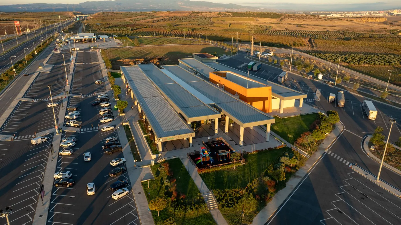 Aerial view of a highway rest area with parking lots beside the mainline at sunset.