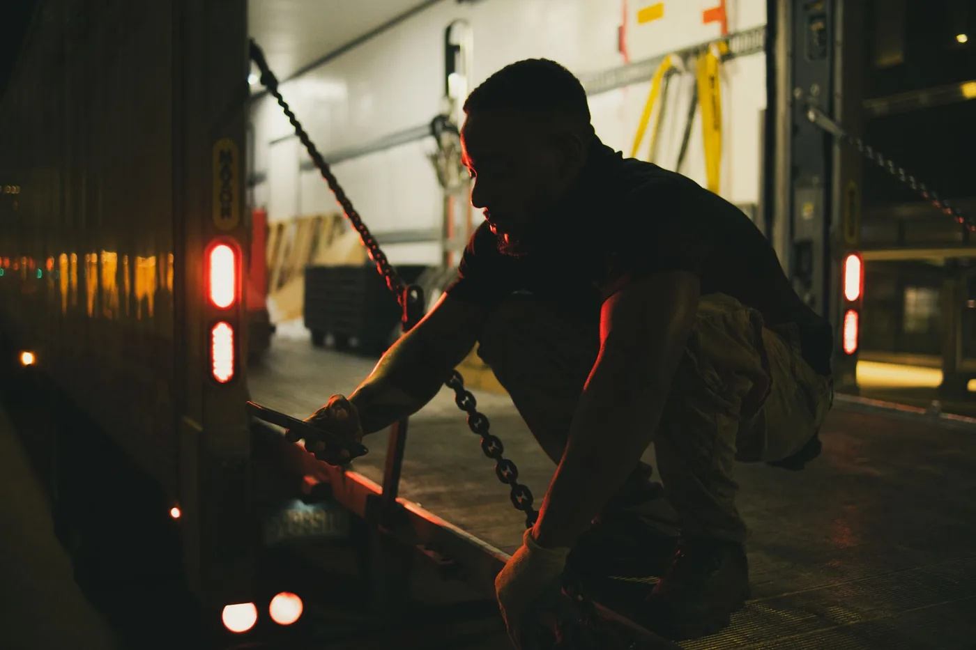 Worker securing chains on a cargo truck at night
