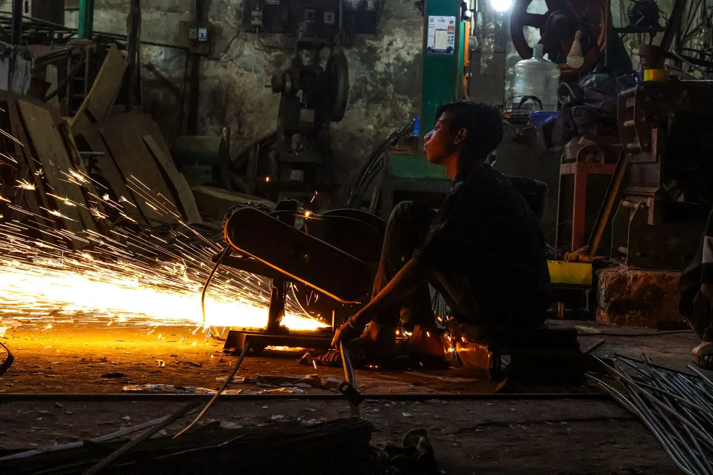 Worker in a dim industrial workshop with sparks coming off the machinery