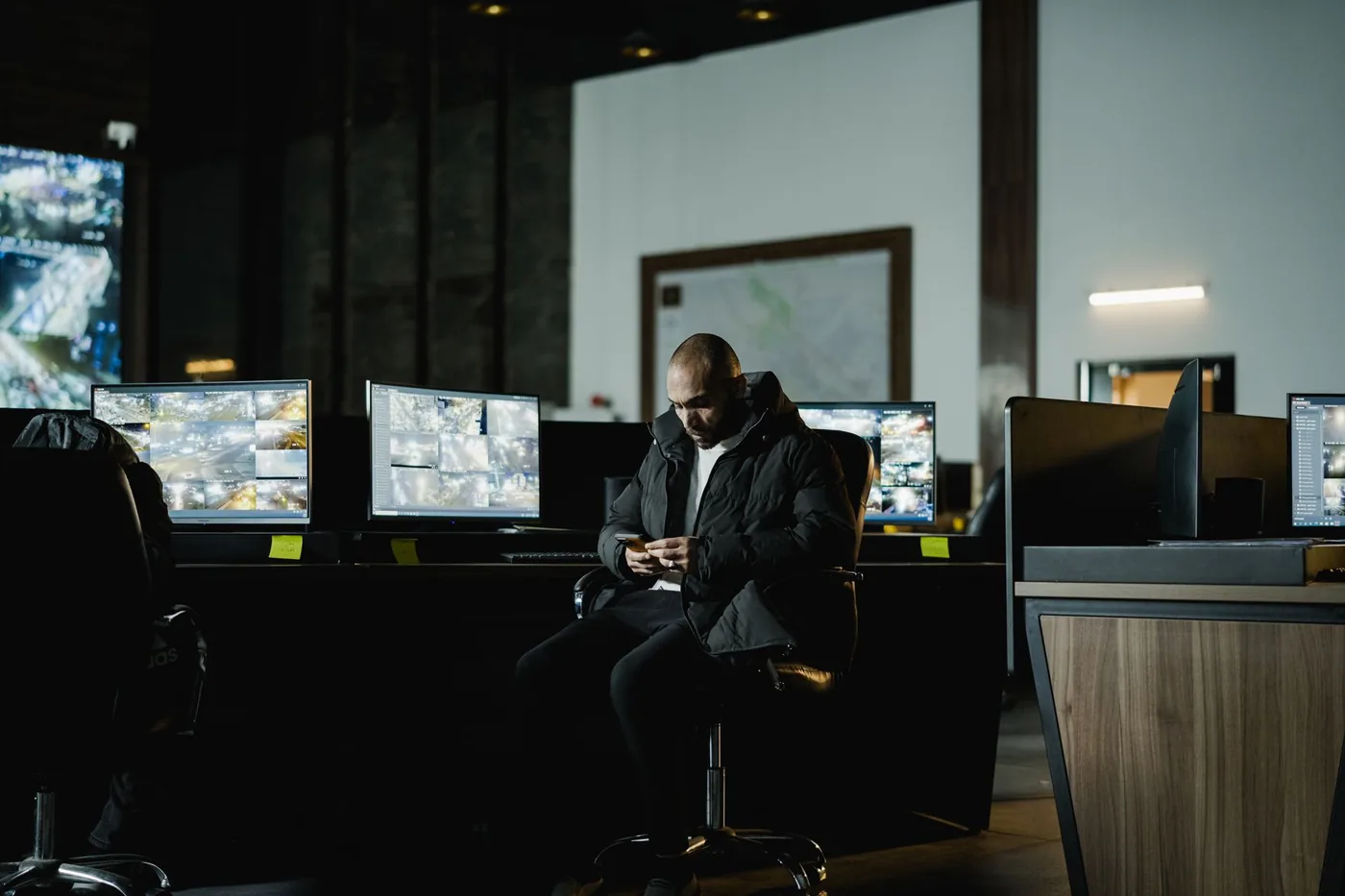 Security officer working a night shift in a dim control room lined with monitoring screens