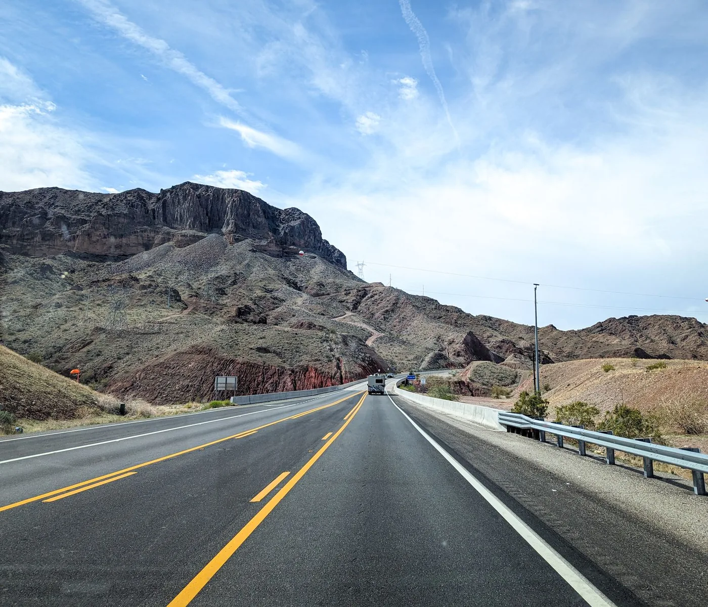 Straight highway stretching ahead through rocky desert toward distant mountains.