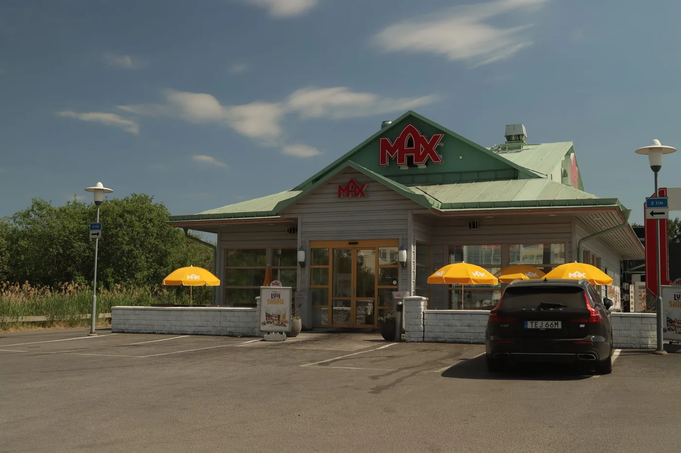 A roadside hamburger restaurant with a parked car on a sunny day.