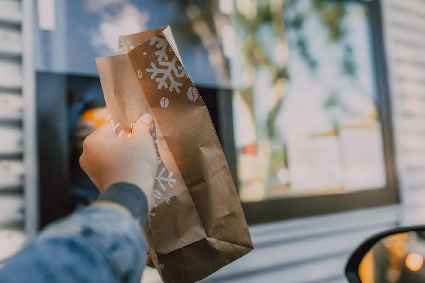 A hand receiving a brown takeout bag at a drive-thru window.