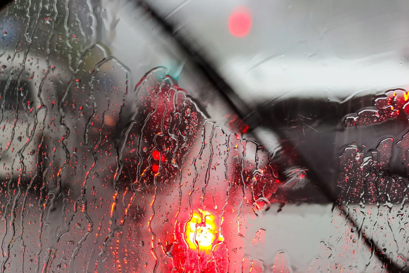 Raindrops on a car windshield with blurred traffic lights on a rainy day.