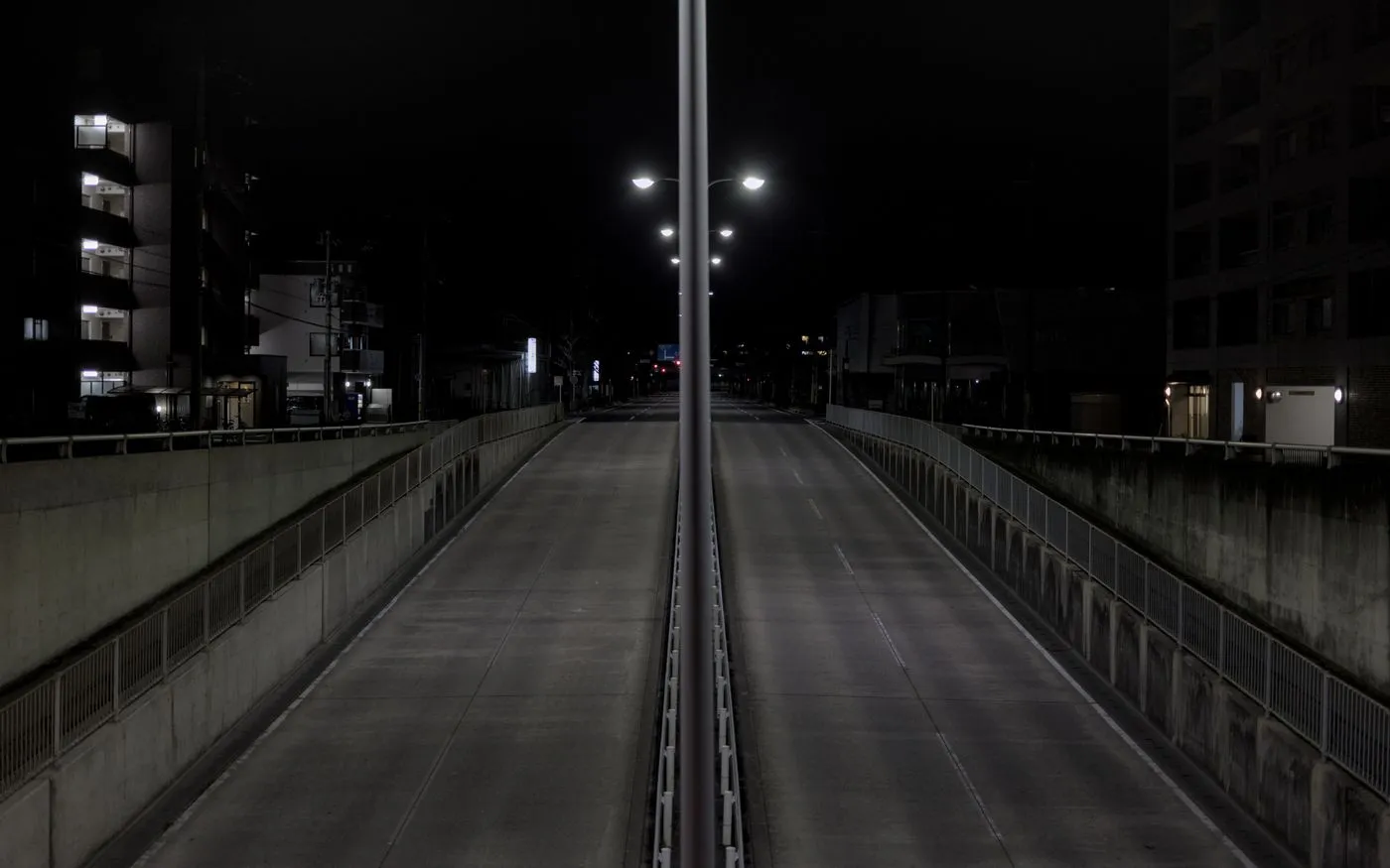 A deserted city highway at night lined with streetlights, like the drive home after a second shift.