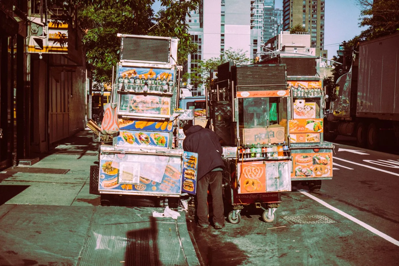 Colorful street food carts lined up on a sunny New York City sidewalk.