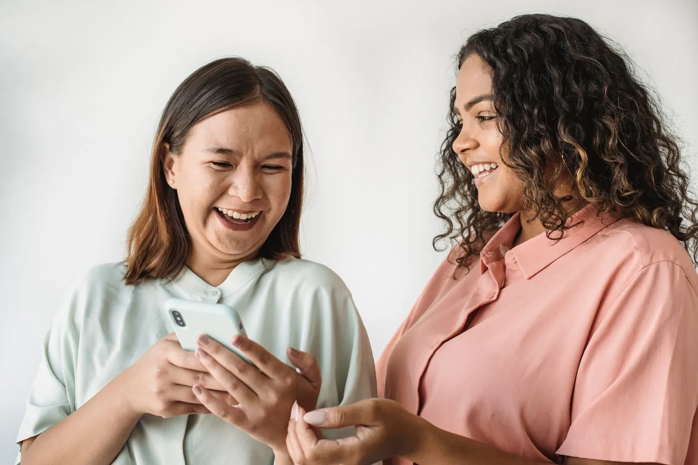 Two women smiling while looking at one smartphone together.