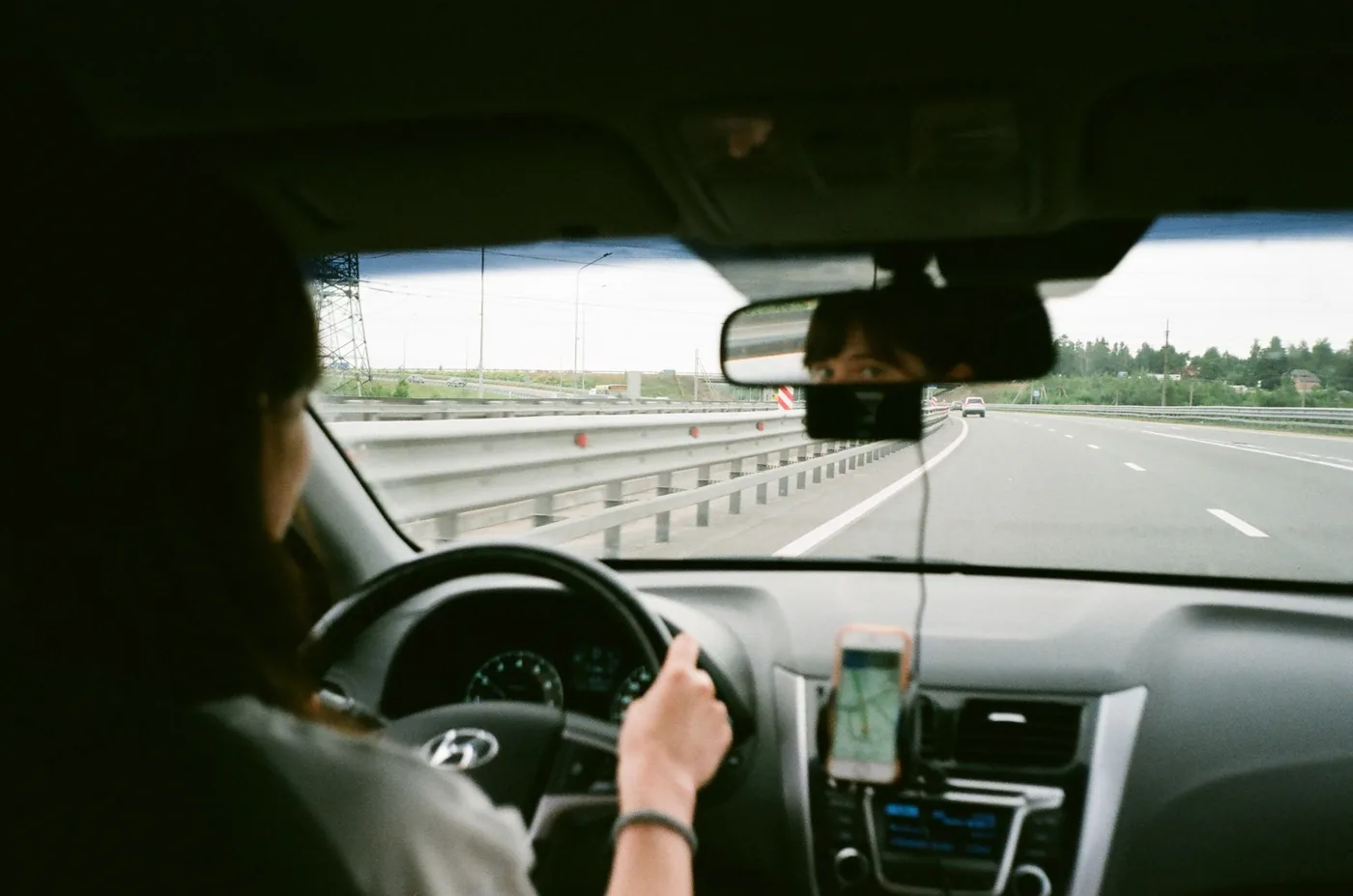 Crop anonymous female holding steering wheel and driving car along asphalt roadway in daytime