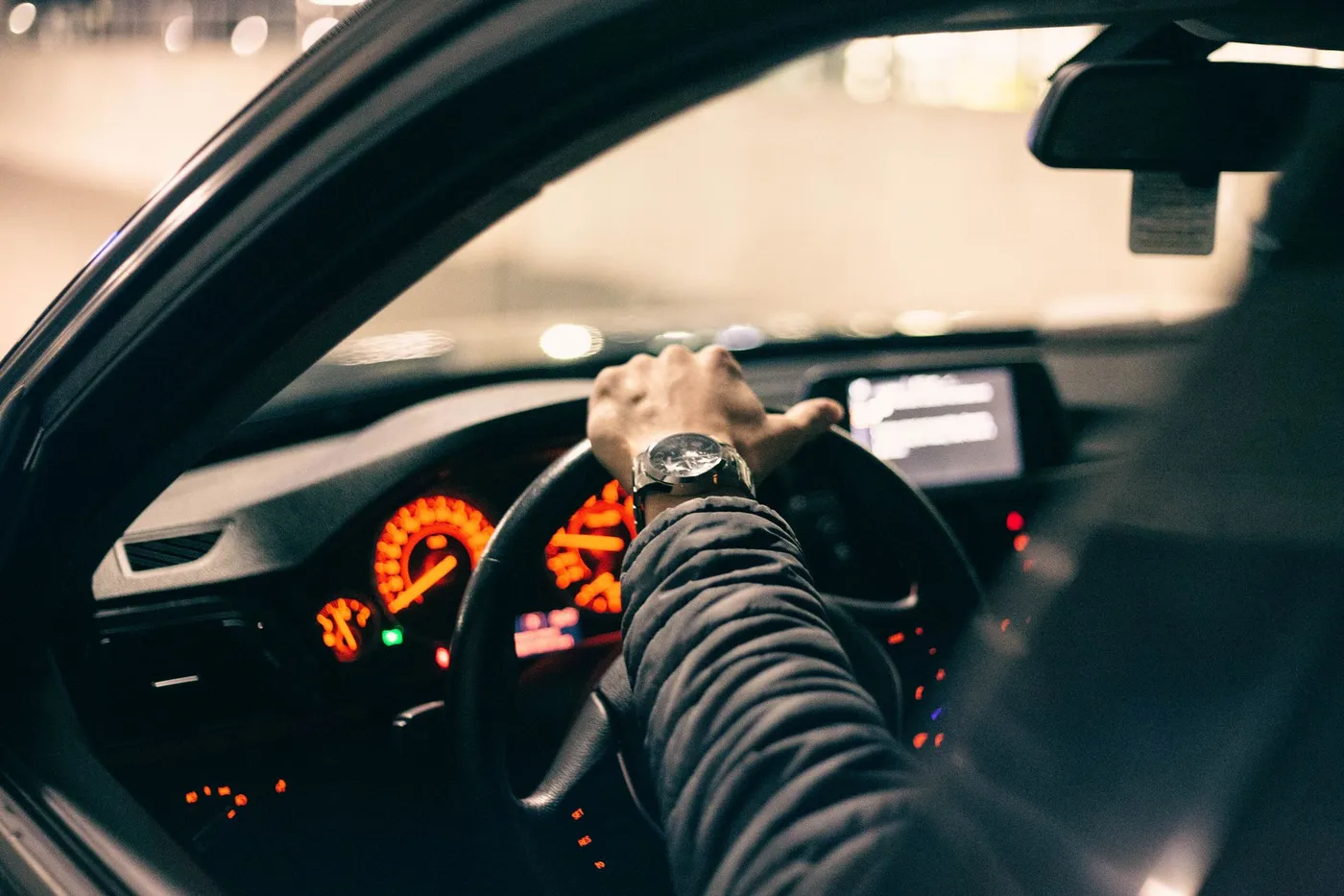 A driver grips the steering wheel at night with the dashboard gauges lit.
