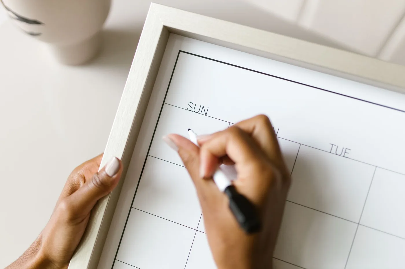Hands writing a shift on a whiteboard wall calendar with a marker